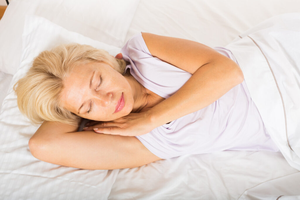 Middle-aged blonde female sleeping on white pillow in bed at home